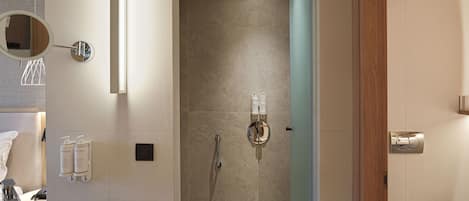 A modern bathroom with a large mirror, a sink, a shower with a glass door, and toiletries on the wall.