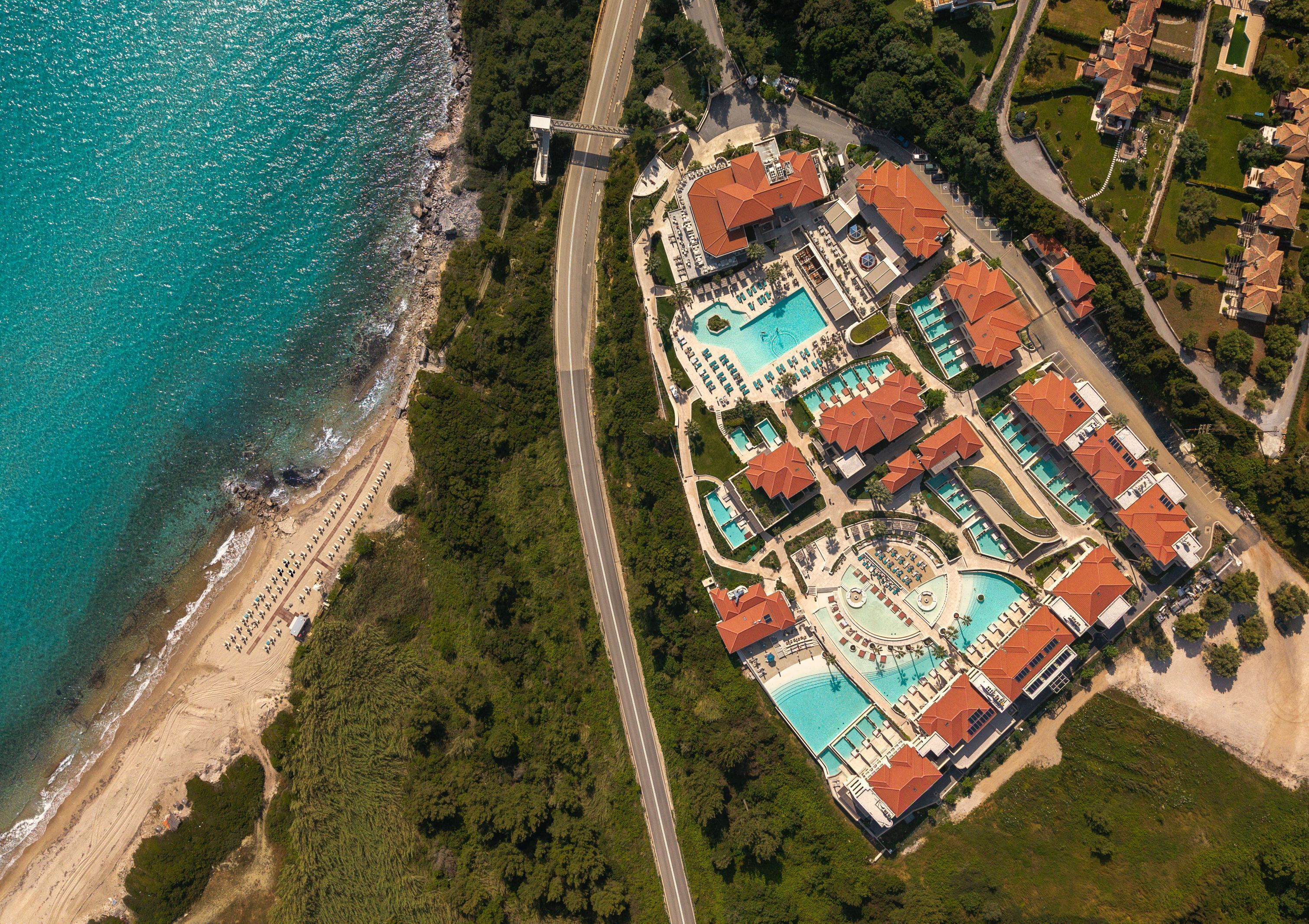 Vista aérea de un complejo turístico costero con una gran piscina, varias villas para huéspedes y una zona de playa.