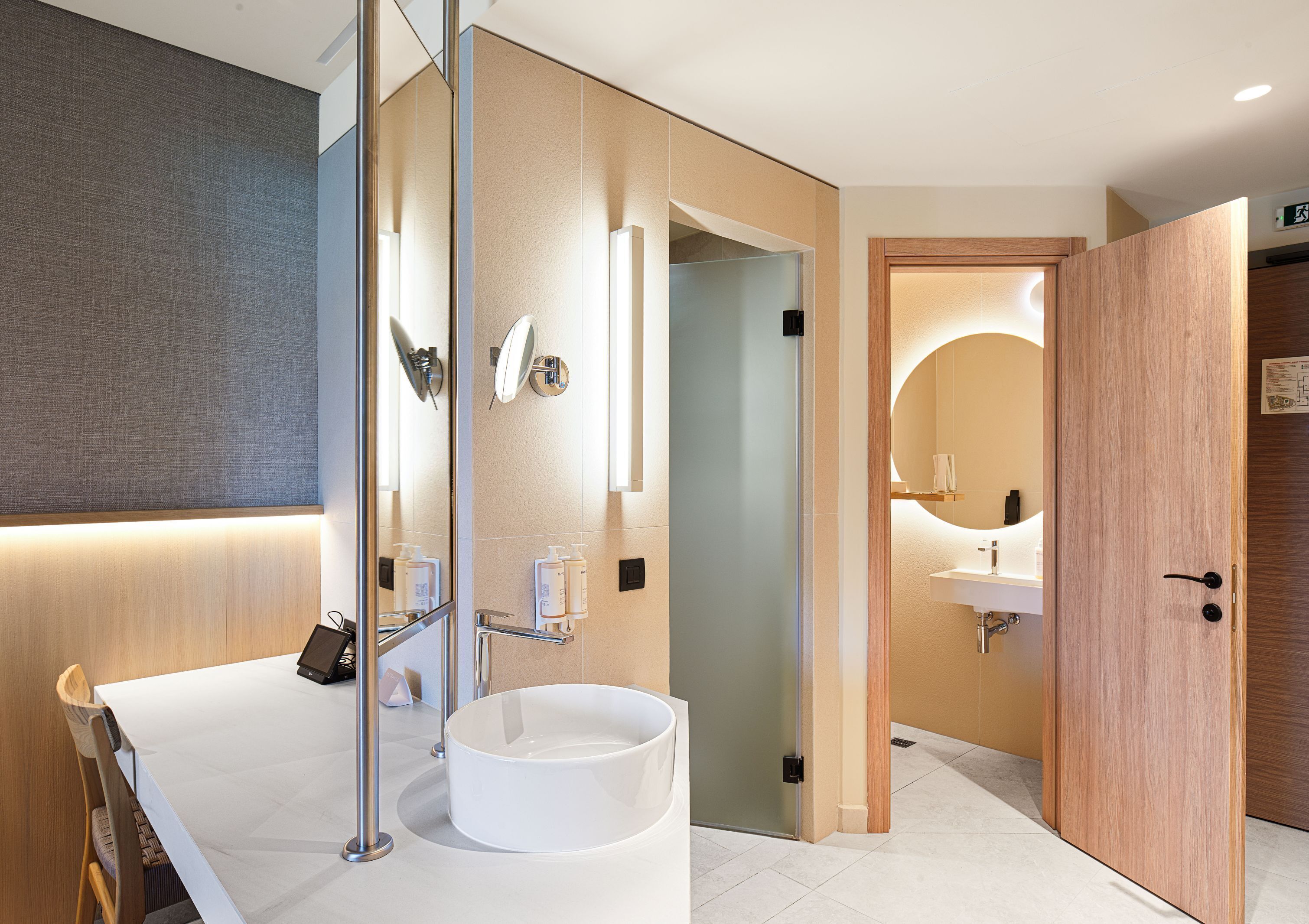 Une salle de bain moderne avec un grand miroir, un lavabo rond et une porte en bois.