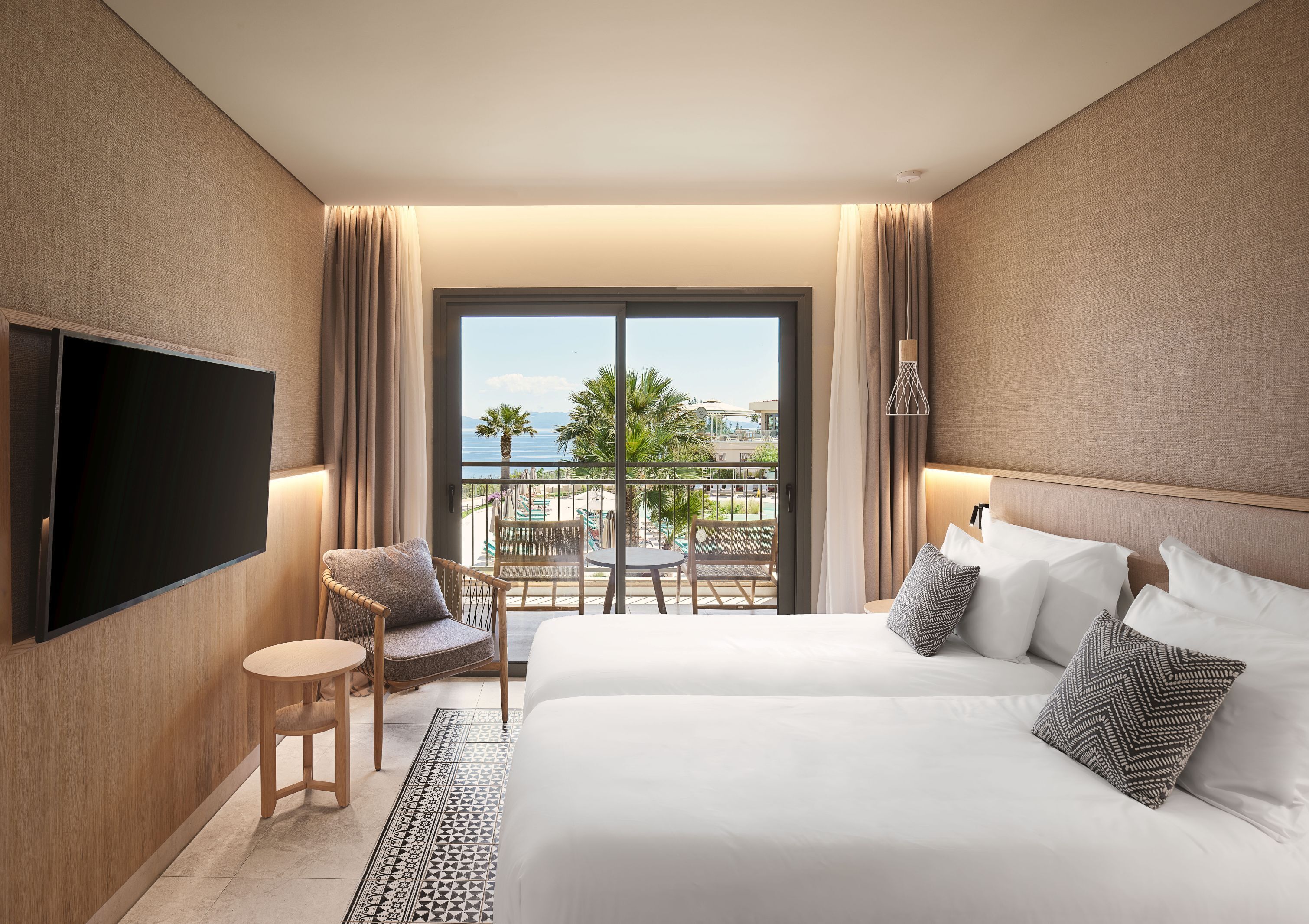 A hotel room with a bed, a TV, a balcony with a view of the sea, and a chair.