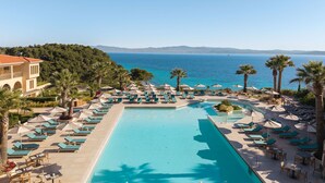 A resort pool with lounge chairs and umbrellas, surrounded by palm trees and a view of the sea. - MERAVIA Leonardo Limited Edition - Adult Only (Kassandra)