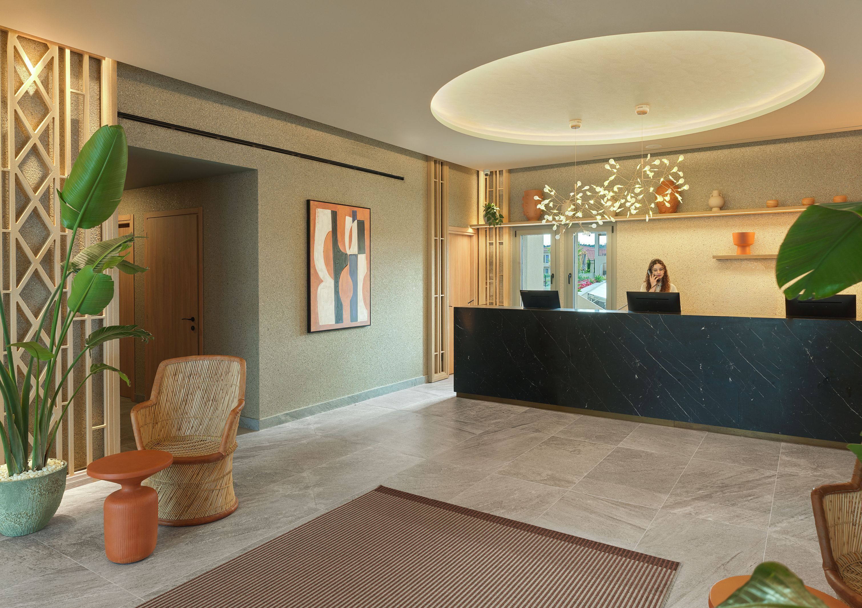 A reception area with a marble reception desk, a large potted plant, a wicker chair, and a framed abstract painting.
