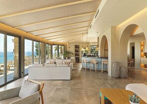 A modern interior with a large seating area, a kitchen with bar stools, and a view of the sea. - MERAVIA Leonardo Limited Edition - Adult Only (Kassandra)