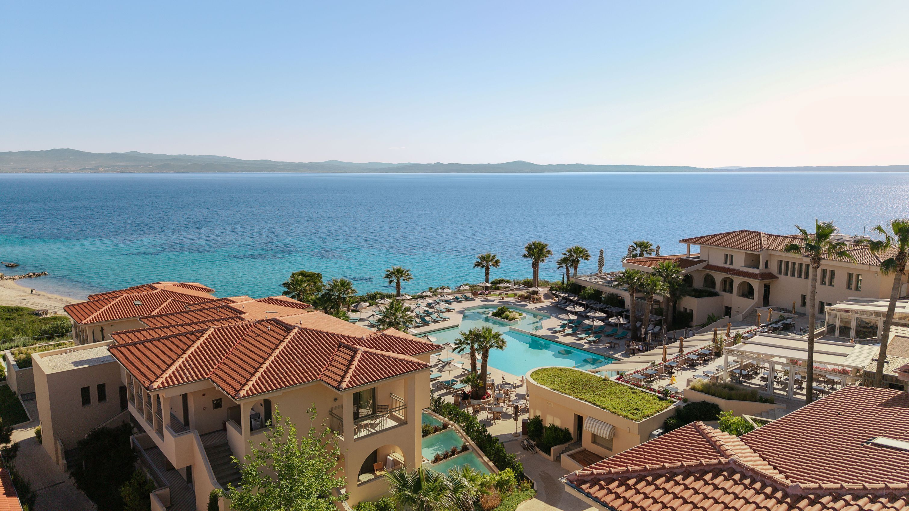 A resort with a pool, palm trees, and a view of the sea.