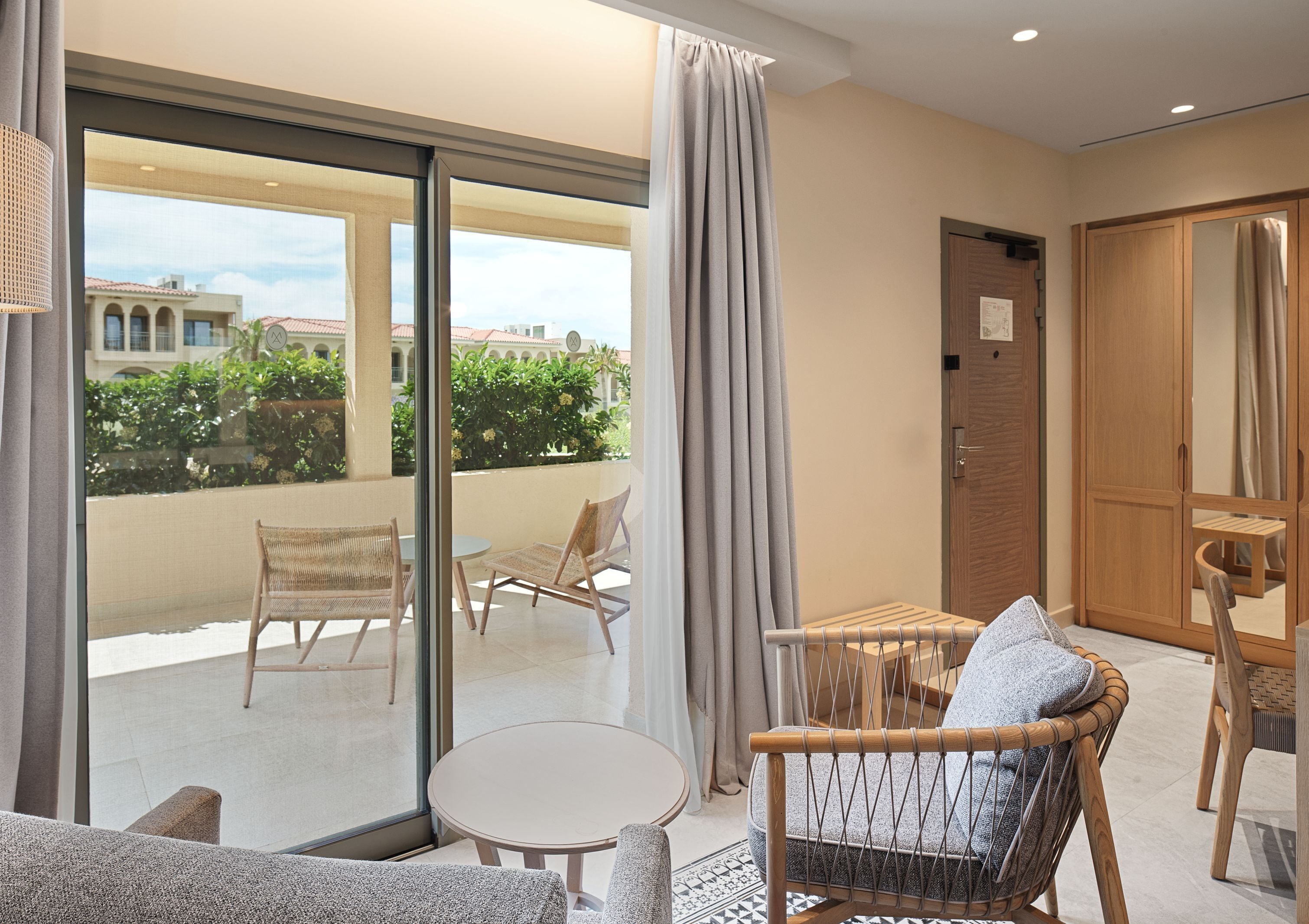 A balcony with wicker furniture, a small round table, and a view of buildings and greenery.
