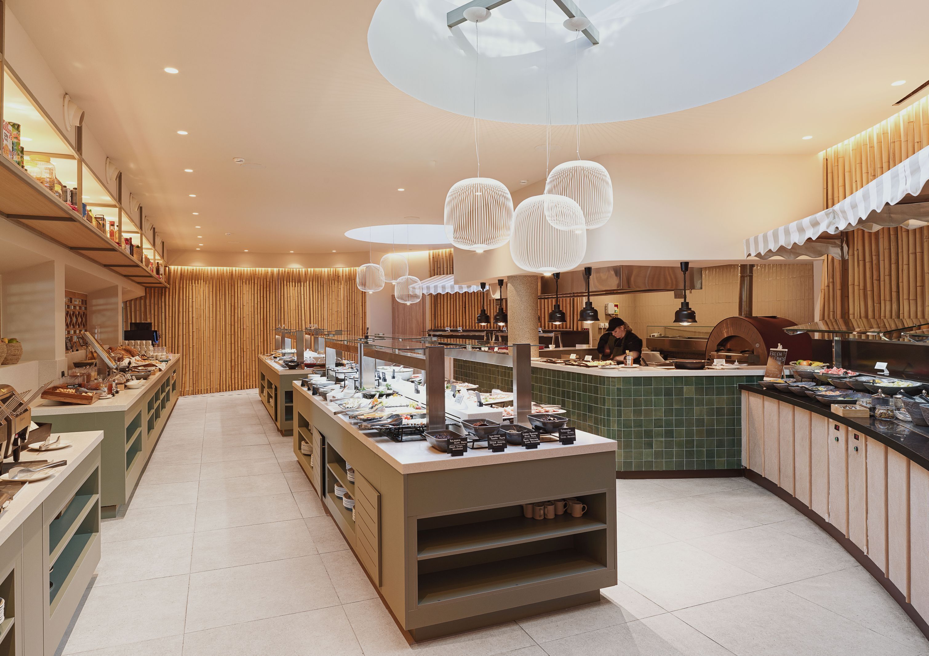 A buffet setup with various food items, a counter with a chef, and hanging light fixtures.