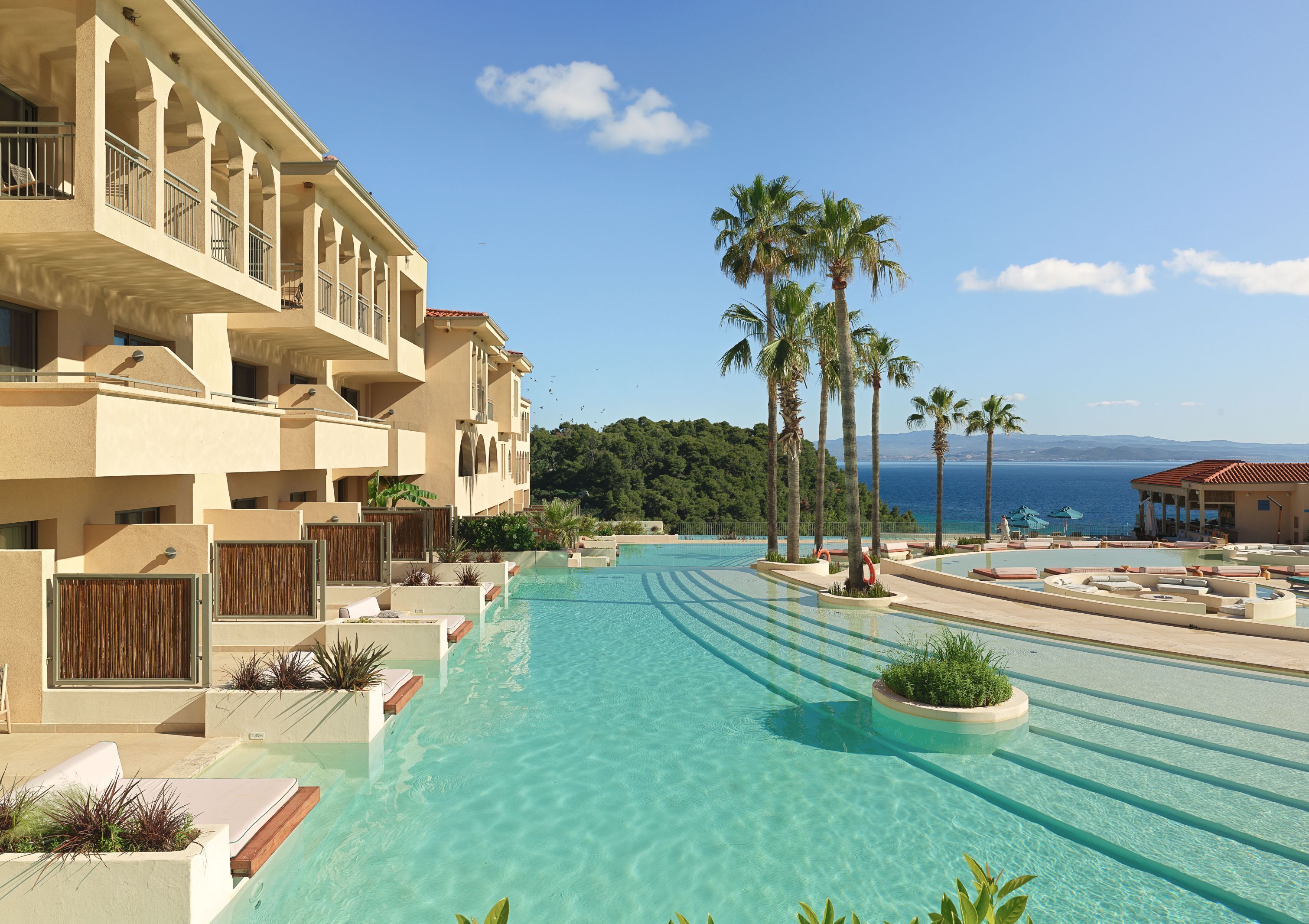 A resort with a large swimming pool, palm trees, and a view of the sea.