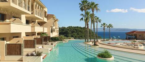 A resort with a large swimming pool, palm trees, and a view of the sea.