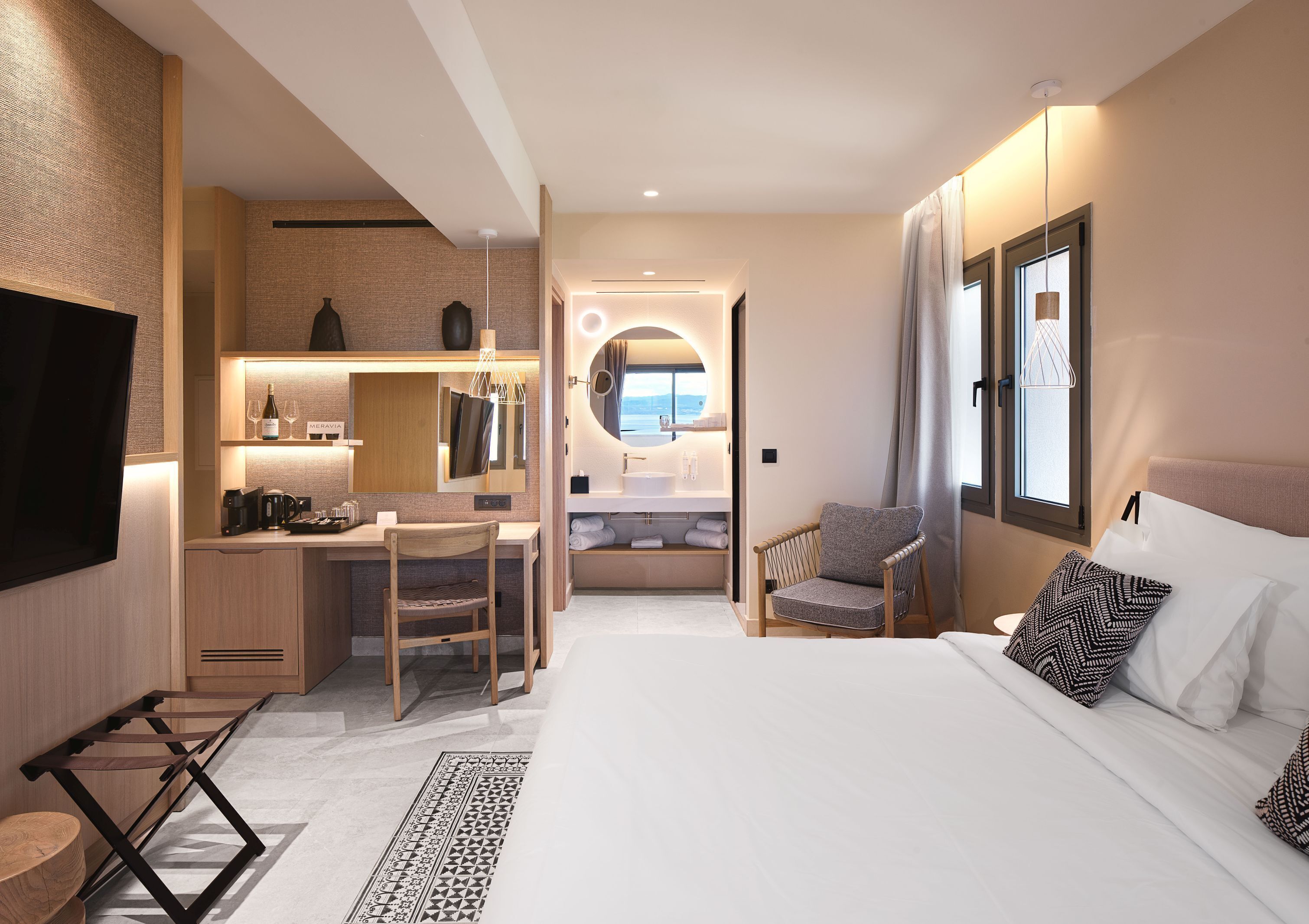 A hotel room with a bed, a desk, a chair, a TV, a bathroom, and a view of the sea.