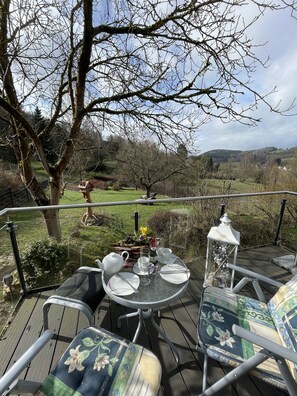 Relax with a cup of tea in this serene outdoor seating area overlooking lush greenery and rolling hills.