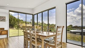 Uma área de refeições com mesa e cadeiras de madeira, grandes janelas com vista para o exterior.