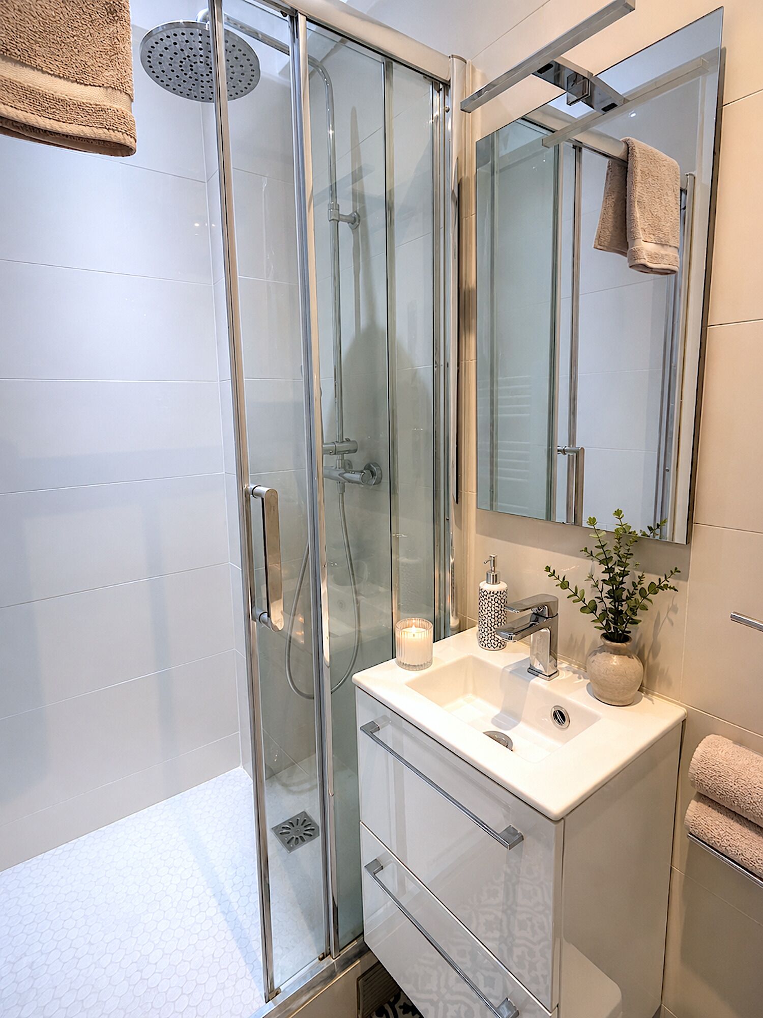 A modern bathroom with a glass-enclosed shower, a white sink, a mirror, and a potted plant.