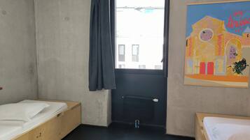 A room with two wooden beds, a window with a curtain, a radiator, and a colorful wall painting.