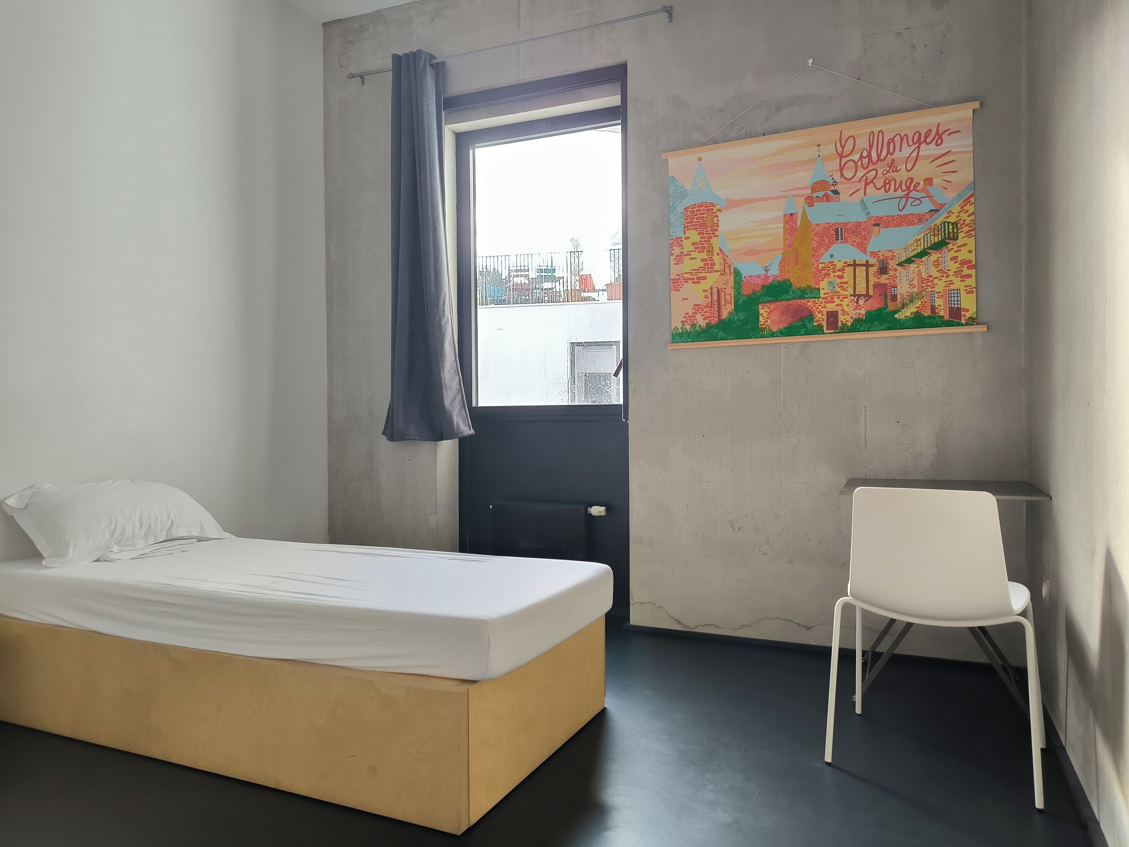 Um quarto com cama, uma cadeira, uma janela com cortinas e uma pintura de paisagem urbana na parede.