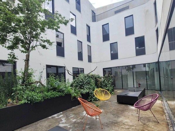 A modern building with multiple windows, a courtyard with greenery, and outdoor seating.