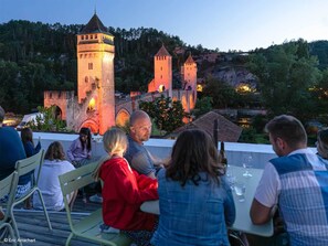 A group of people dining at an outdoor table with a view of a castle and surrounding greenery.