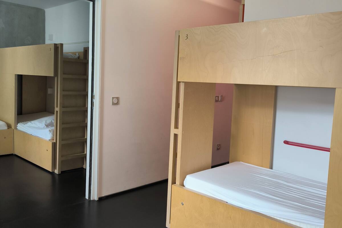 Une chambre de dortoir avec des lits superposés, une armoire et une porte donnant sur une autre pi èce.