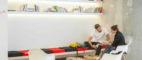 A modern reading area with a bench, chairs, and a bookshelf filled with books.