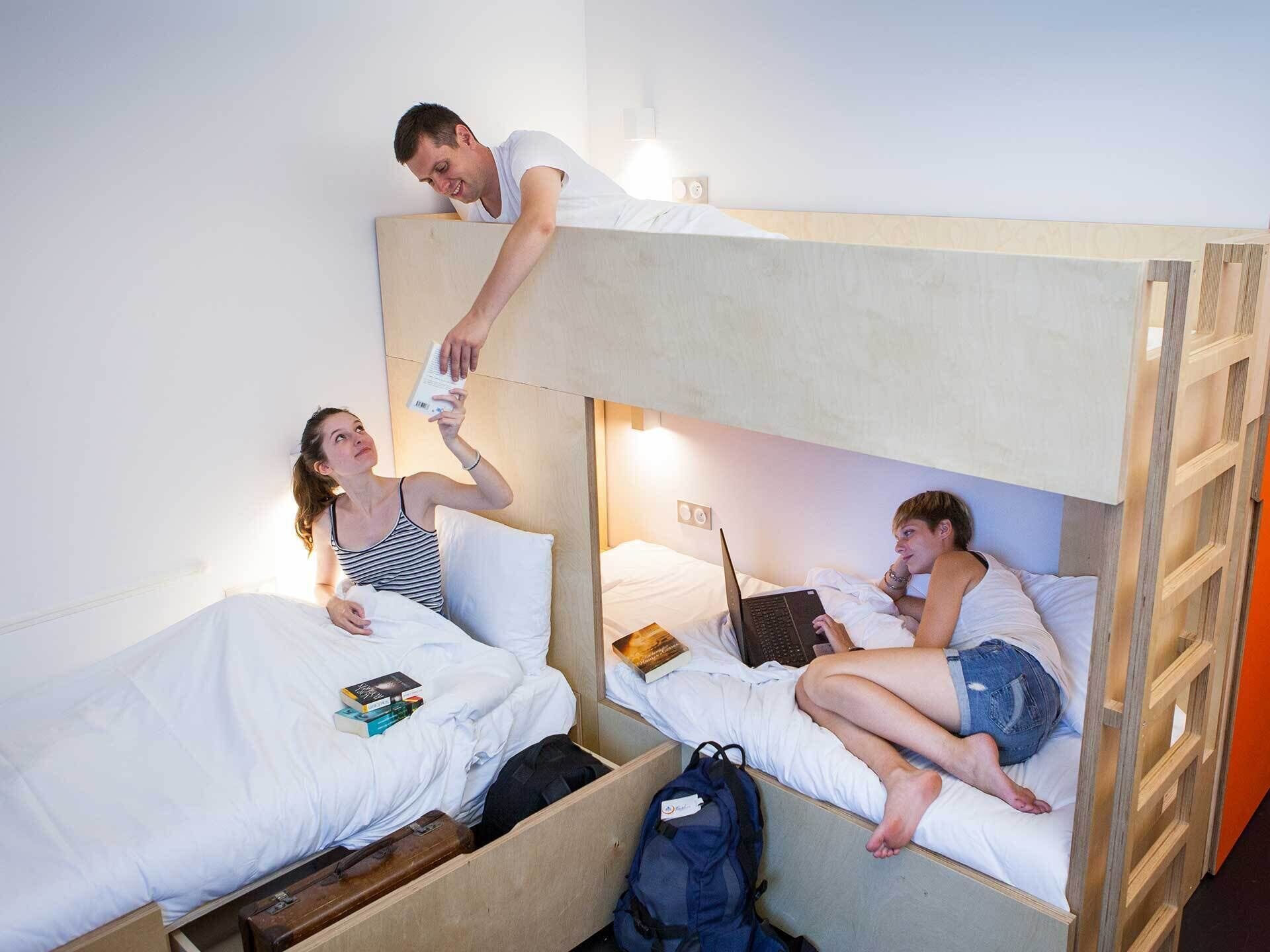 Une chambre avec un lit superposé, chaque lit étant occupé par une personne. Il y a des livres et un ordinateur portable sur les lits.