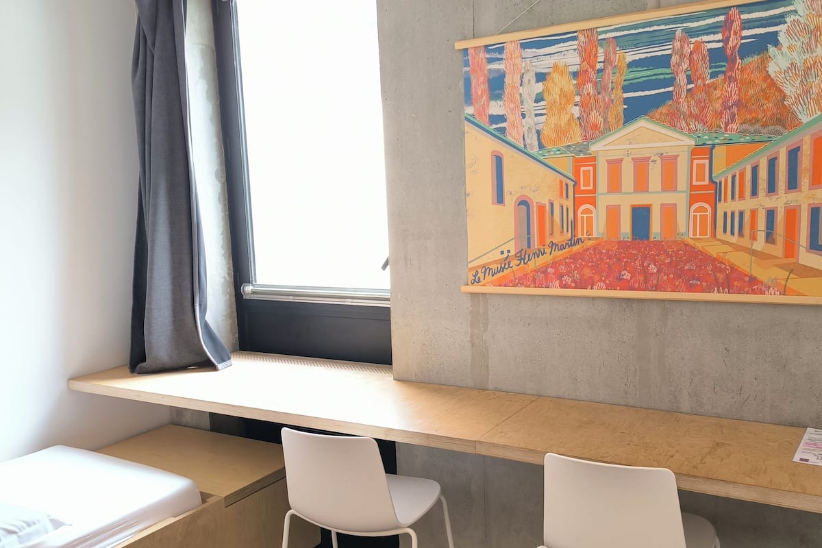 Une pièce avec une fenêtre, un tableau, un bureau et deux chaises.