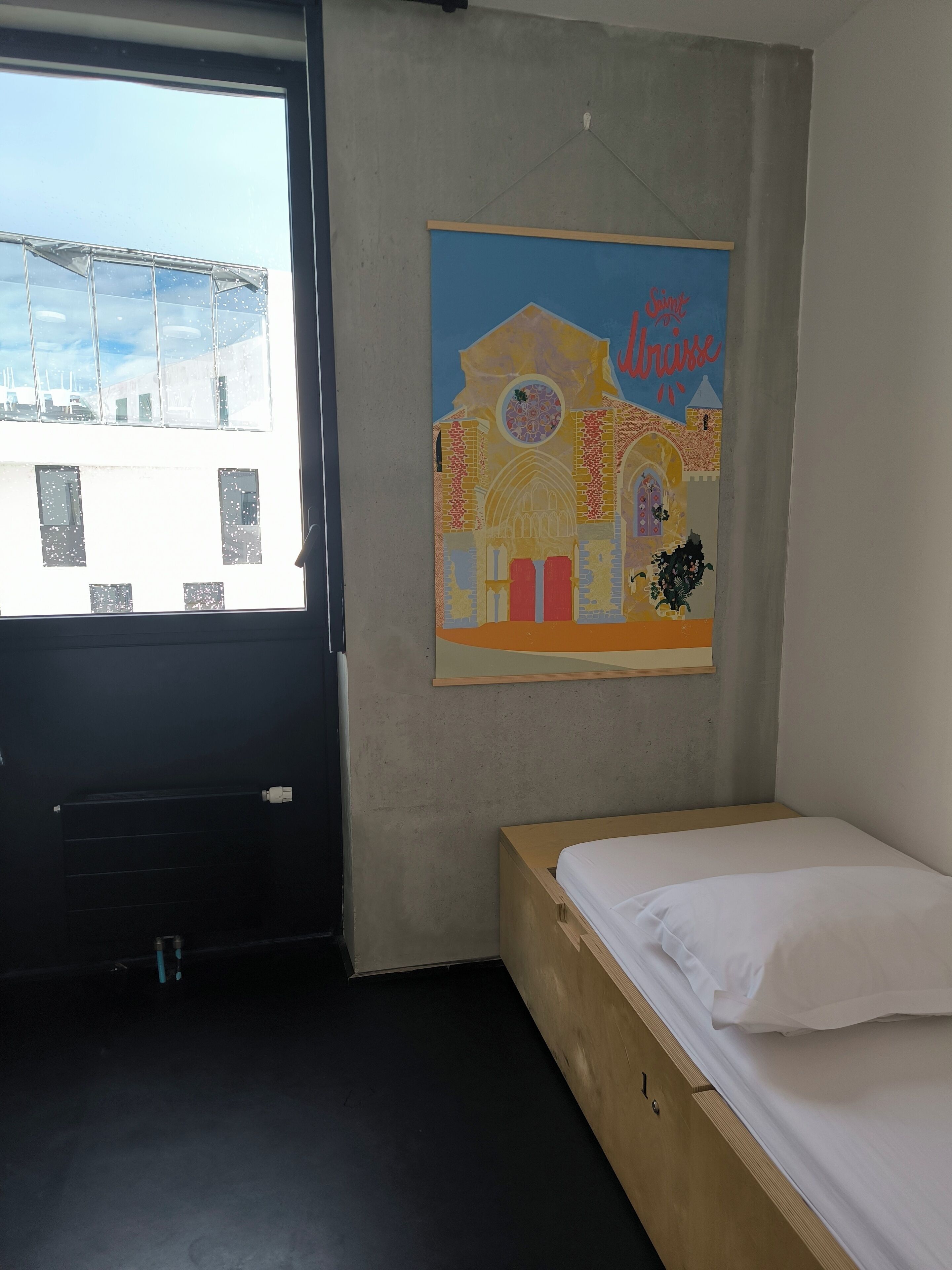 Une pièce avec un lit, une fenêtre et un tableau accroché au mur.