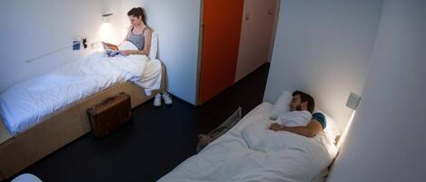 Una habitación de residencia estudiantil con dos camas, una maleta y una mesita.