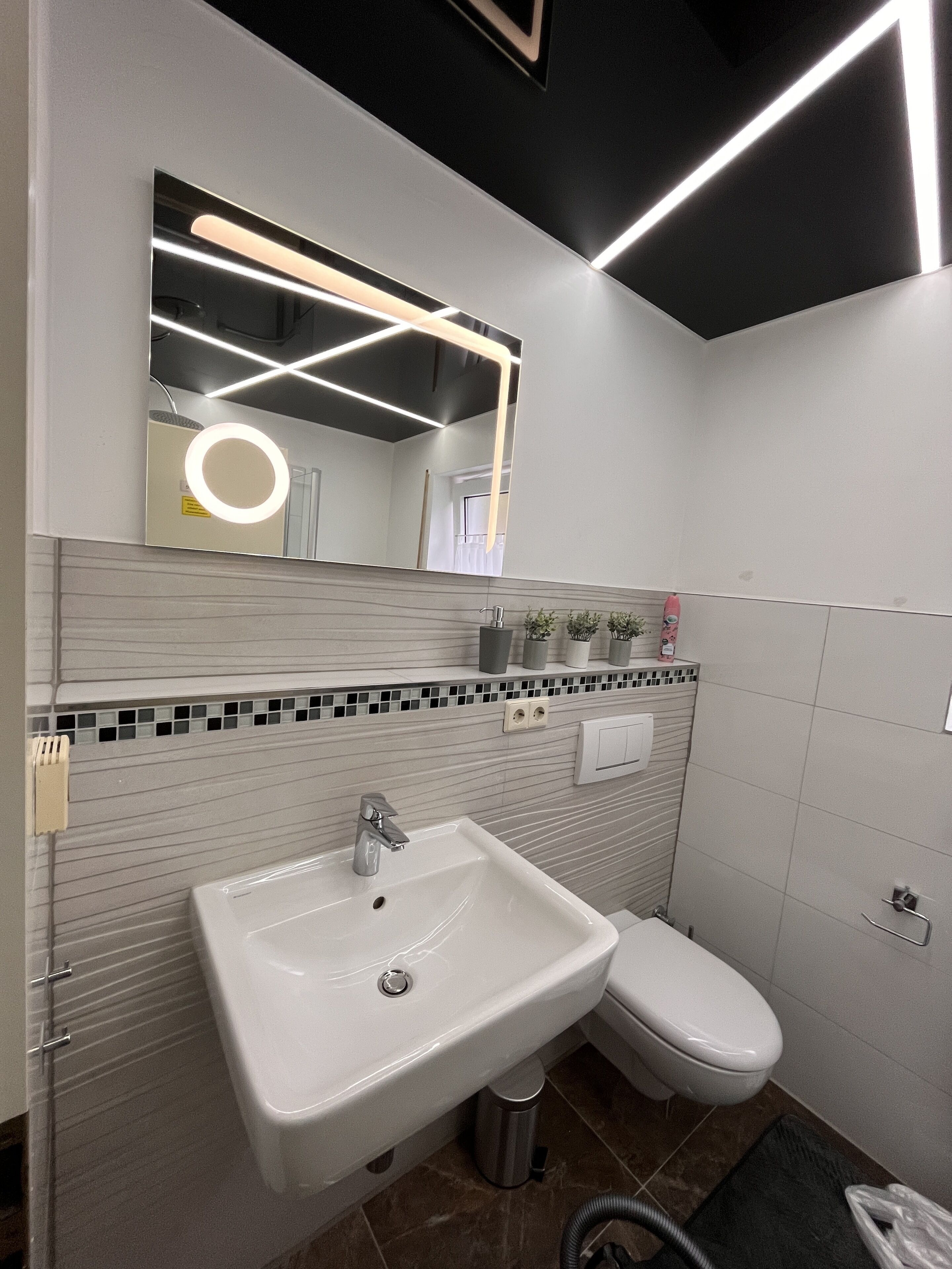 Une salle de bain moderne avec un lavabo blanc, un miroir doté d’un anneau lumineux et des toilettes.