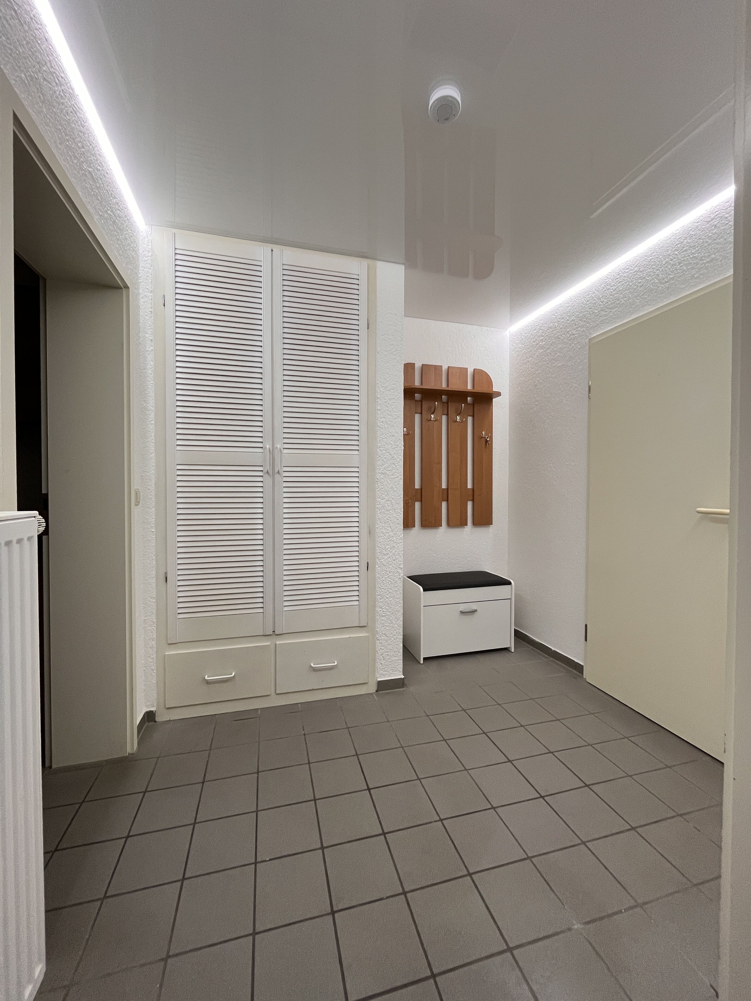 A hallway with a white wardrobe, a small bench, and a coat rack.