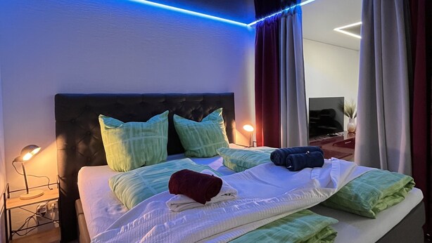 A modern bedroom with a large bed, a nightstand, and a wall-mounted lamp. - Apartment with terrace, 48sqm. for max. 4 persons (Bühlertal)