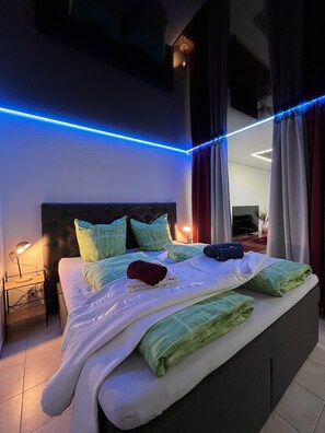 A modern bedroom with a large bed, a nightstand, and a wall-mounted lamp.