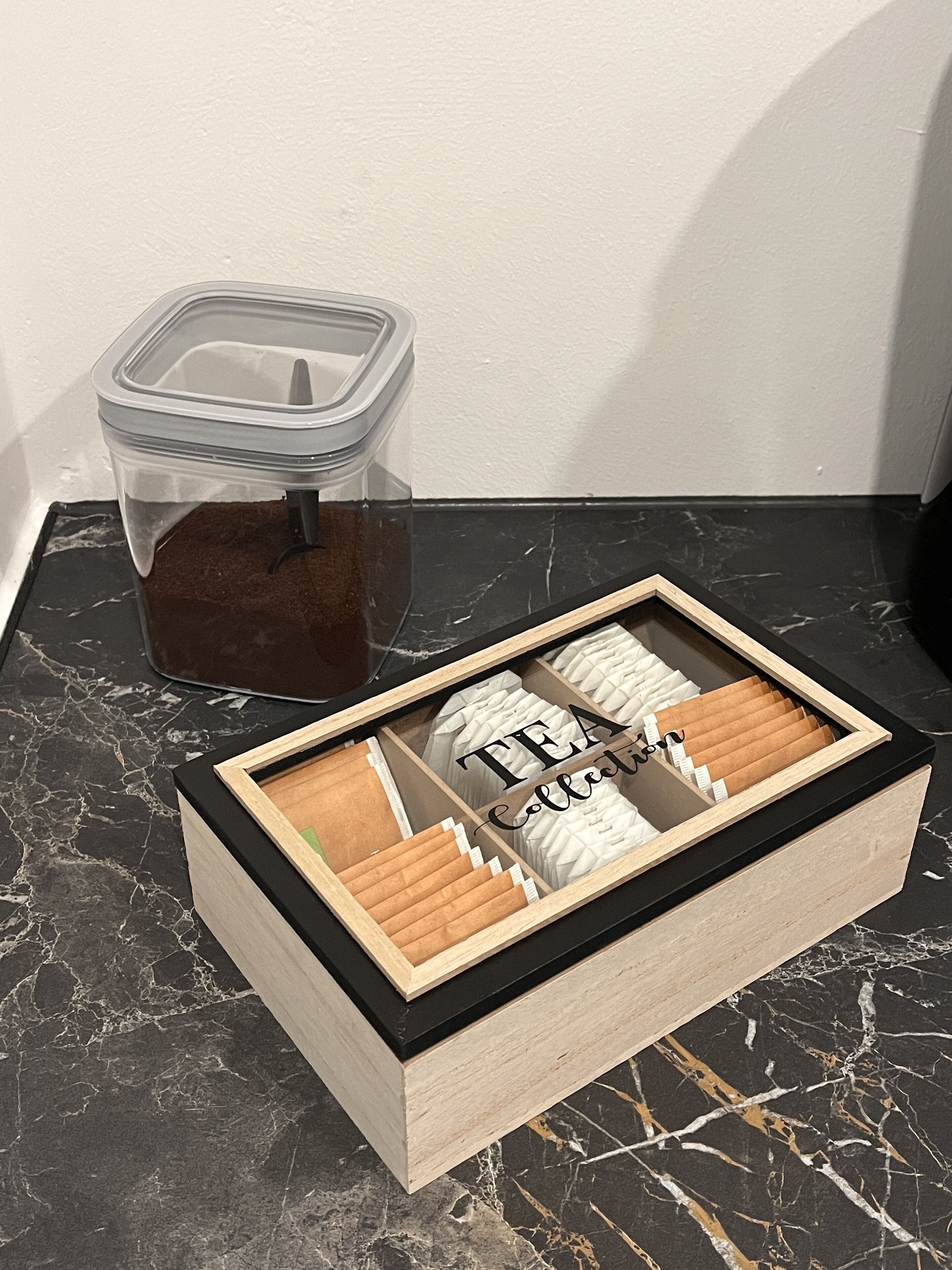 A wooden box with compartments containing tea bags and a transparent container with a tea bag.