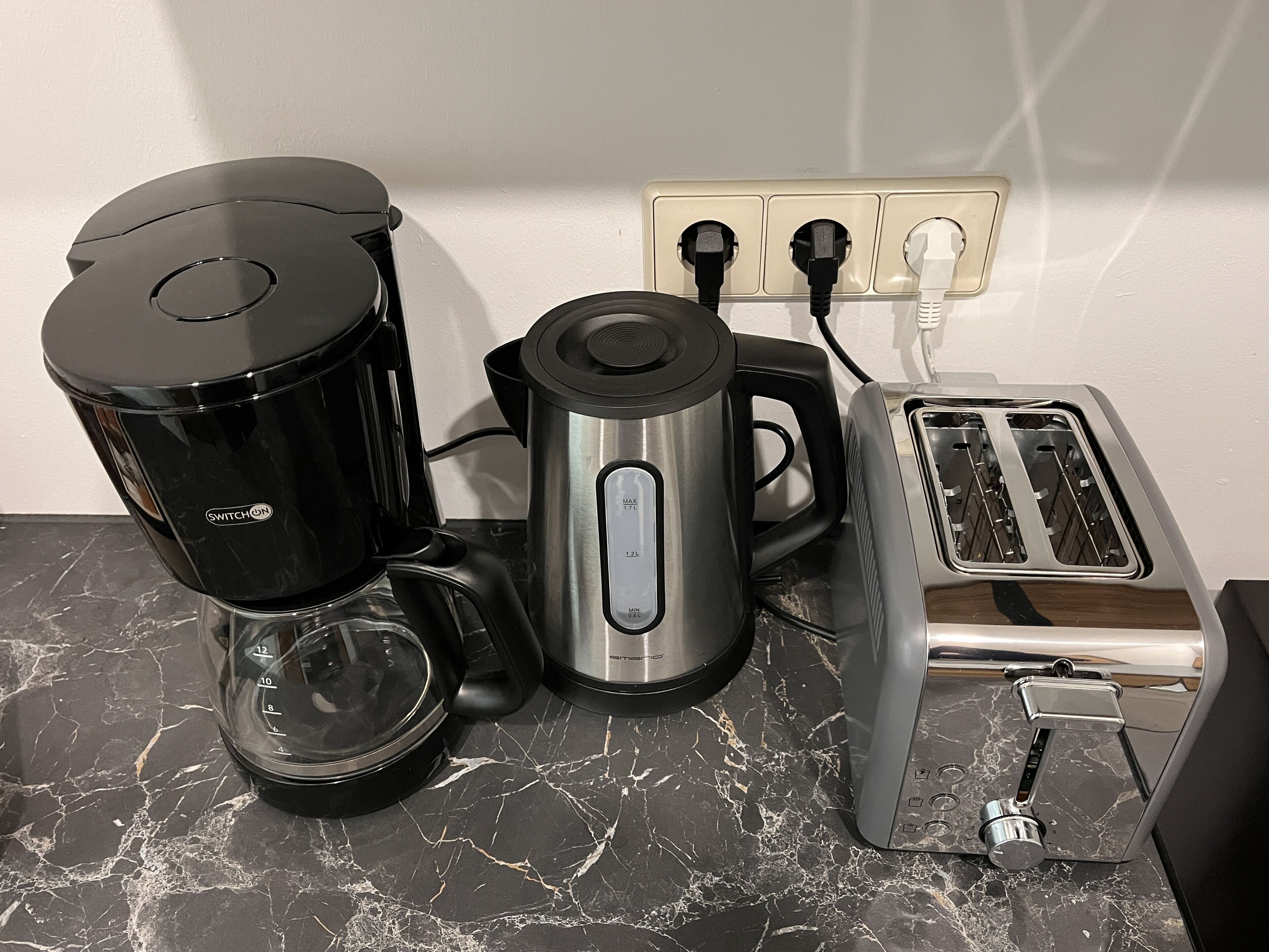 A kitchen with a coffee maker, a kettle, and a toaster on a marble countertop.