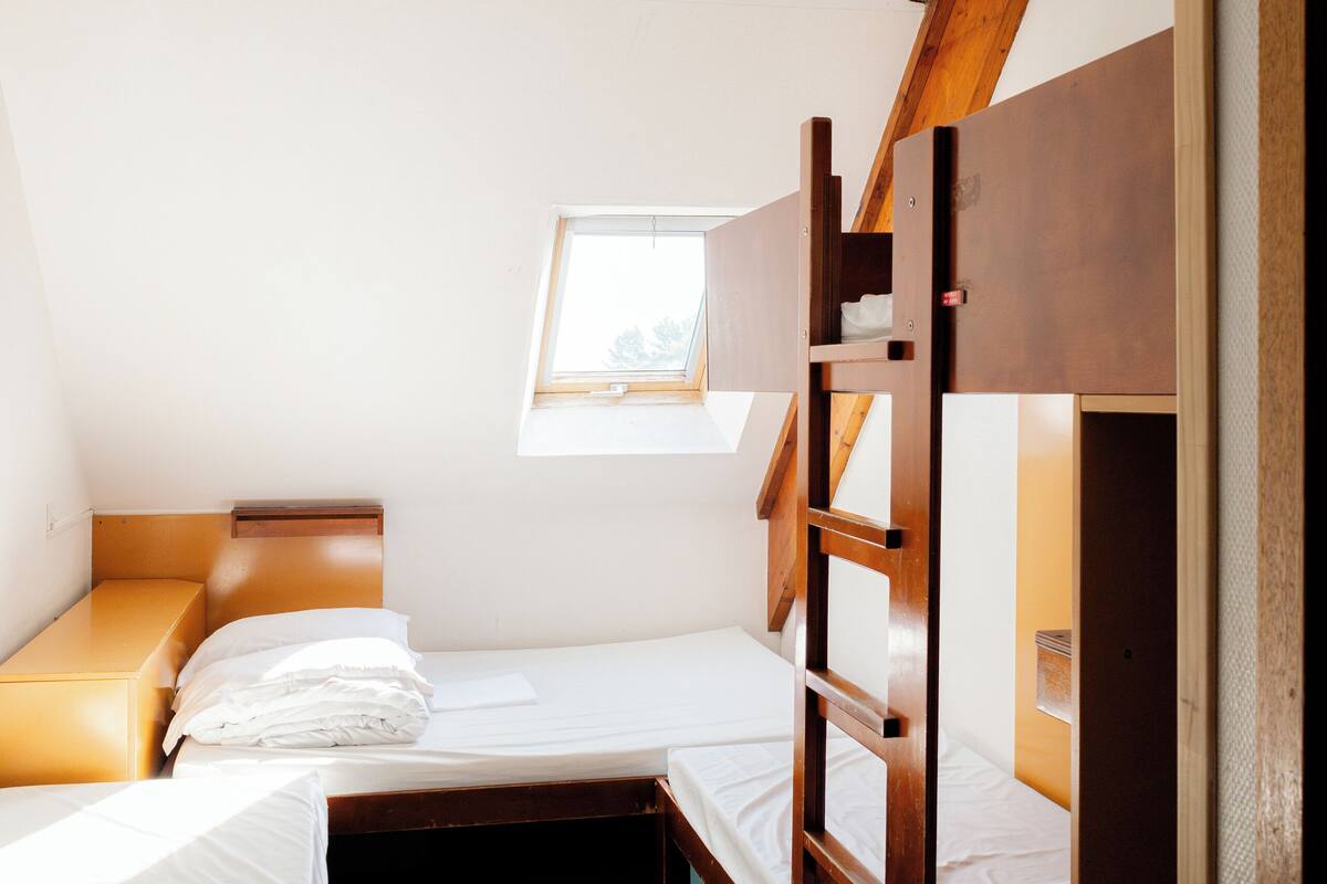 Un dormitorio con literas, una ventana pequeña y techo inclinado.
