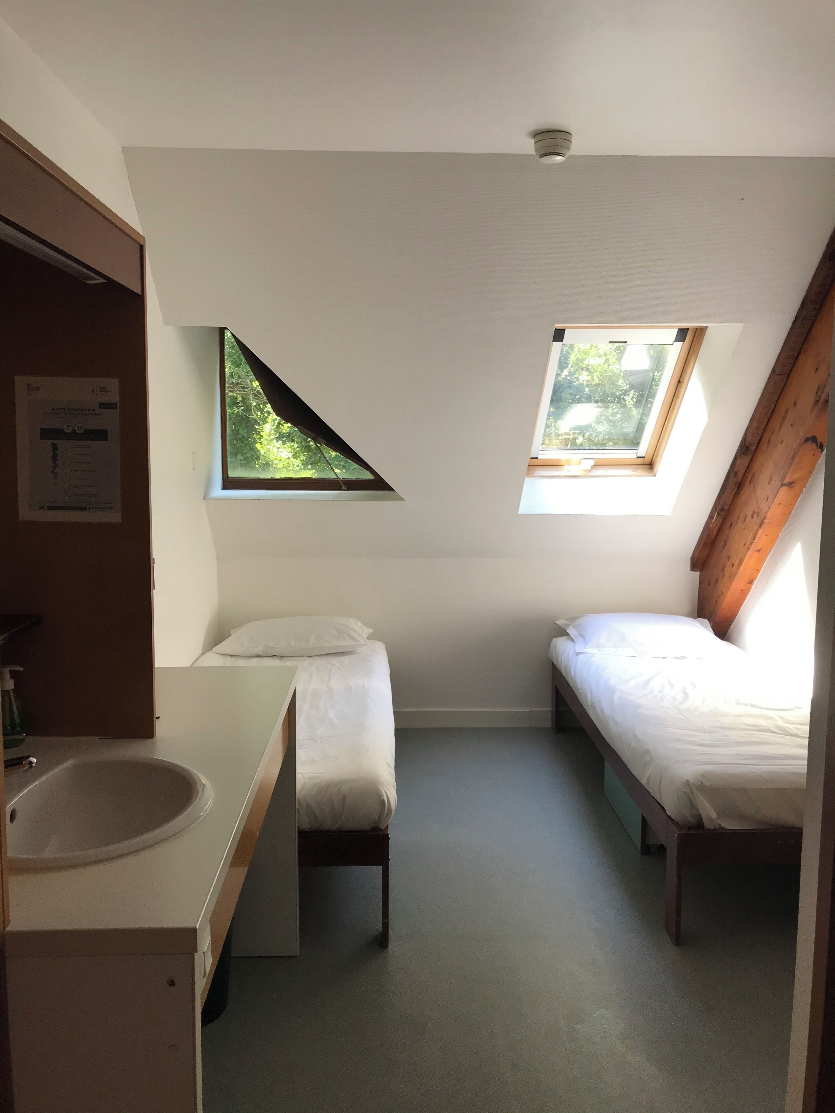 Une petite pièce, de taille modeste, comprenant deux lits, une fenêtre et un lavabo.