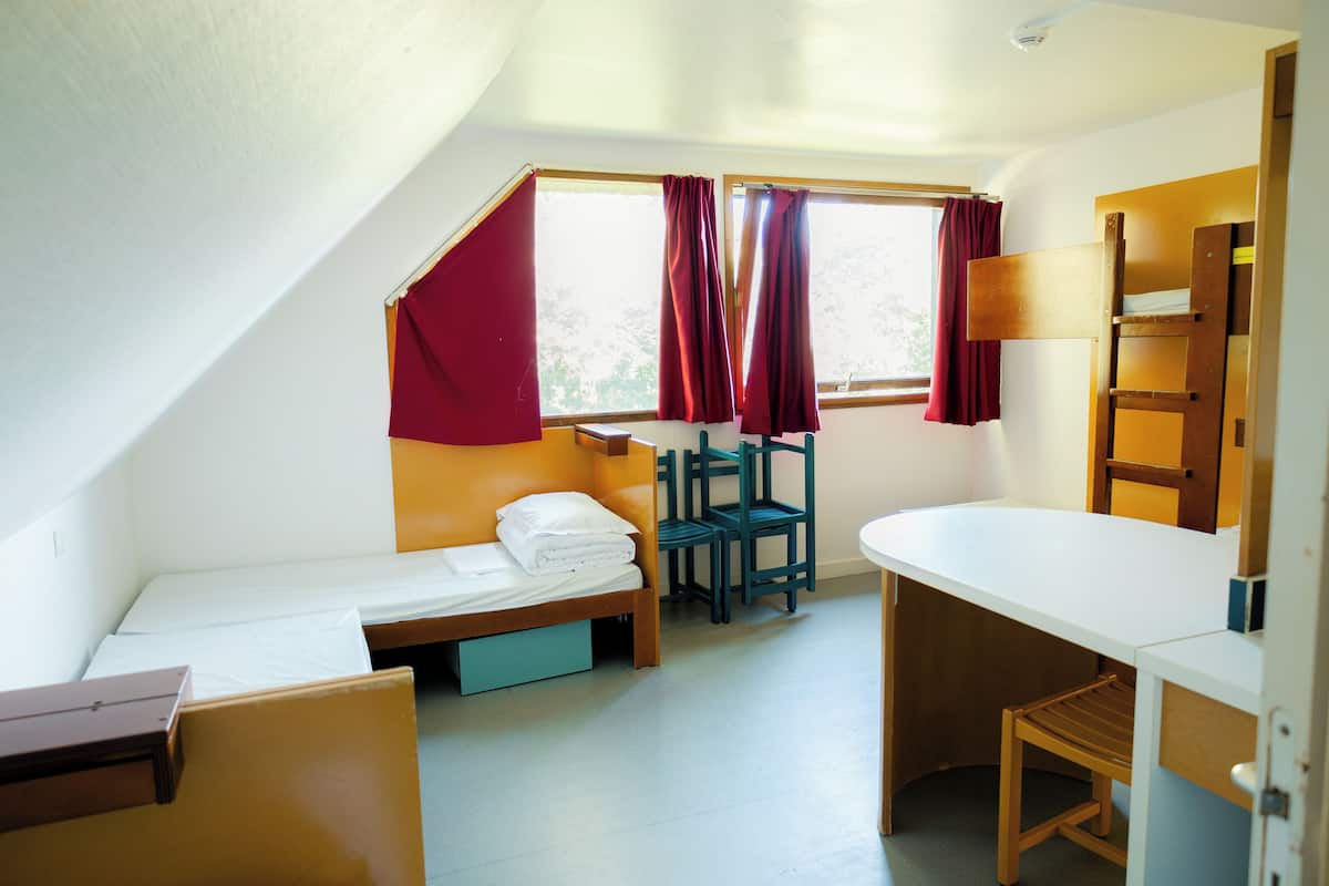 Una habitación tipo dormitorio con una cama individual superpuesta, un escritorio, una silla y una ventana con cortinas.