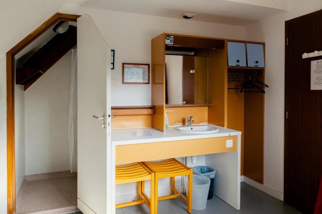 Casa de banho compacta com lavatório, espelho e banqueta de madeira.