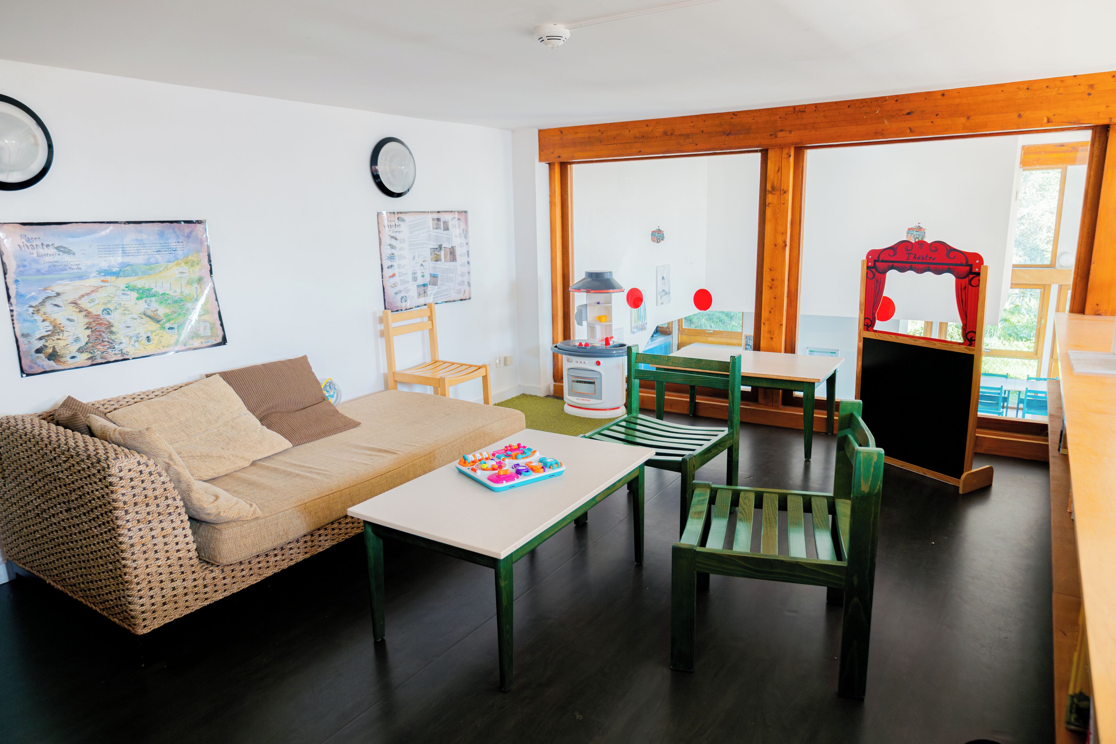 Una sala de estar acogedora con un sofá, una mesita y un sillón verde. Se ve una ventana con vistas a árboles y una cortina roja.