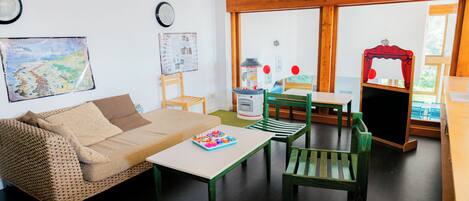Una sala de estar acogedora con un sofá, una mesita y un sillón verde. Se ve una ventana con vistas a árboles y una cortina roja.