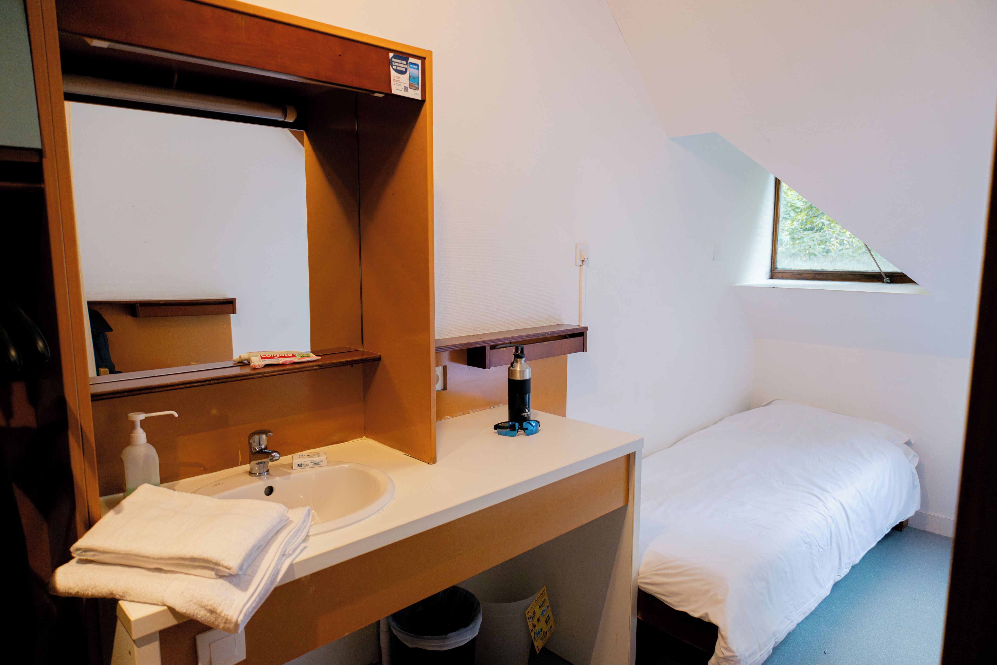 A small, tidy room with a single bed, a white sink, and a mirror above it.