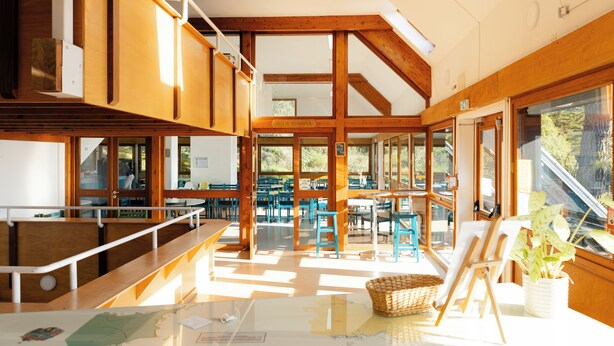 Un comedor amplio con vigas de madera, ventanas grandes y sillas azules.