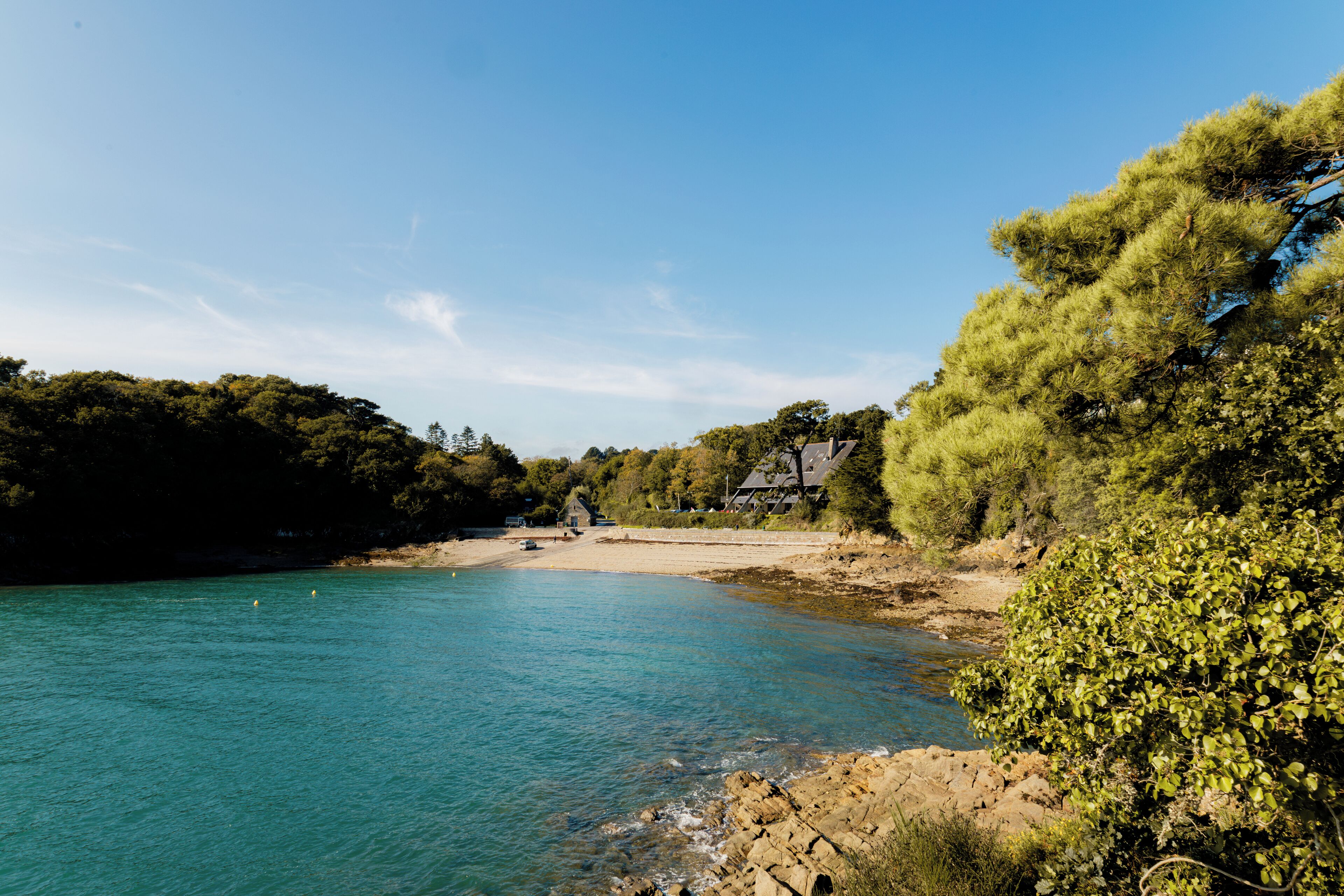 A coastal landscape with a clear blue sea, sandy beach, and a house with a sloped roof.