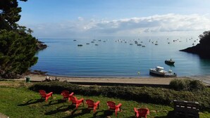 Vista costera con playa, sillas rojas y barcos en el agua.