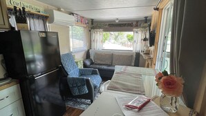 Ett kompakt bostadsutrymme med ett litet kök, en soffa, ett matbord med papper och ett kylskåp.