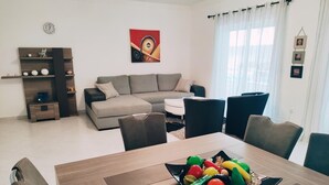 Un salon moderne avec un canapé, une table à manger et des chaises. Il y a une horloge au mur et un tableau au-dessus du canapé.