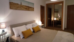 Une chambre à coucher comprenant un lit, des tables de chevet, une lampe, un tableau et une porte coulissante donnant sur une salle de bain.