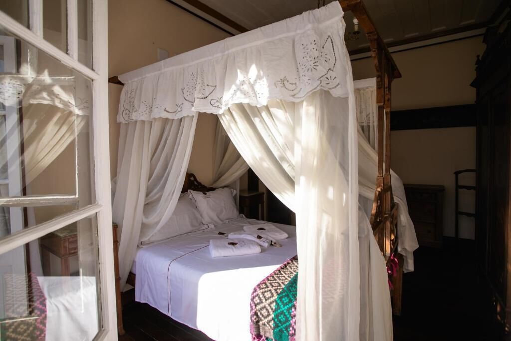Un letto a baldacchino con tende, biancheria bianca, una coperta decorata e una testiera in legno.
