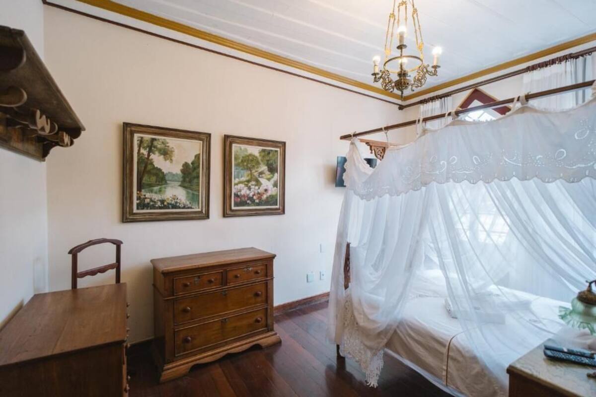 Une chambre à coucher avec un lit à baldaquin, une commode en bois et deux tableaux représentant des paysages, encadrés et accrochés au mur.