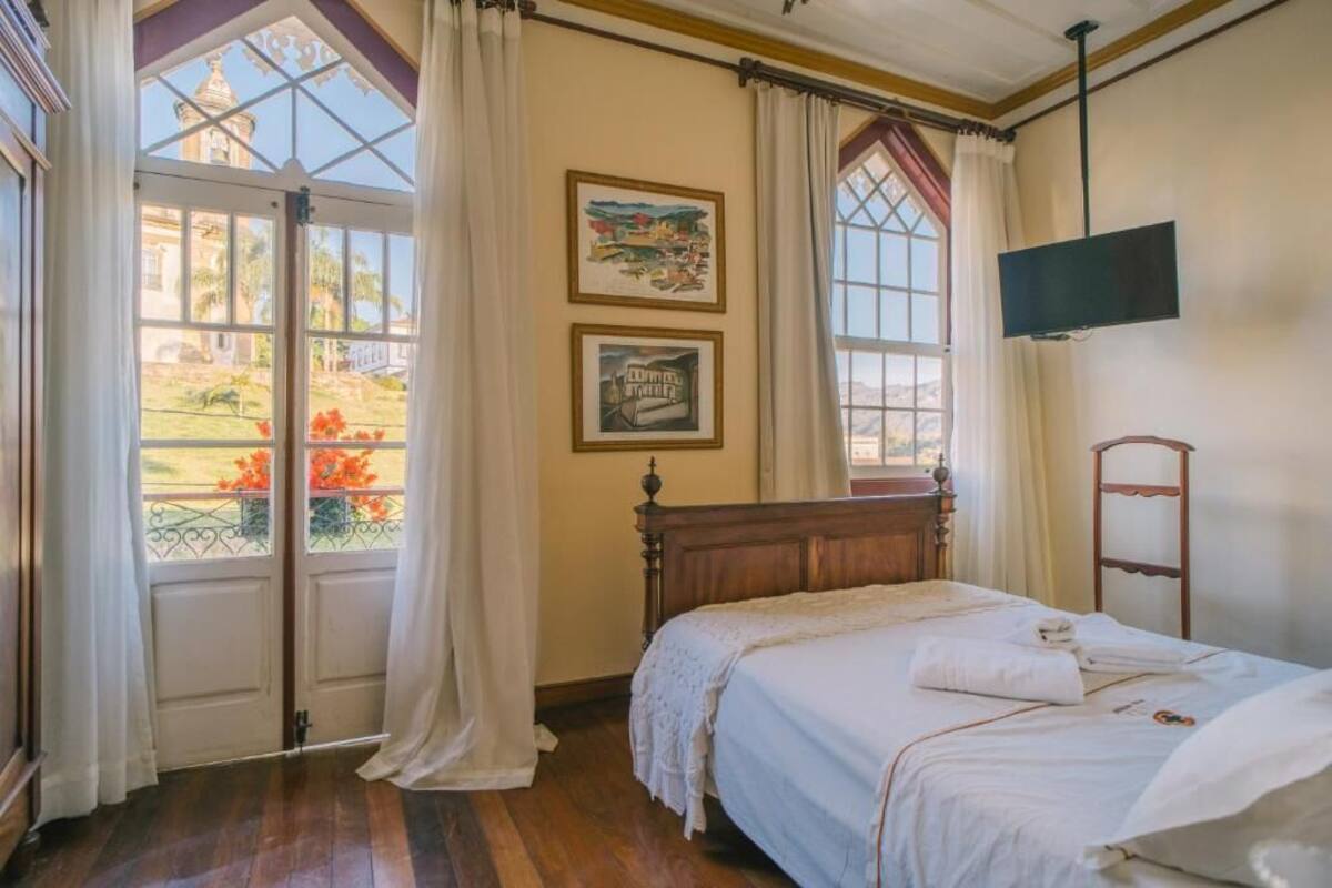 Une chambre avec un lit en bois, un téléviseur fixé au mur et une fenêtre avec des rideaux.