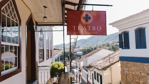 Rua estreita com edifícios tradicionais, um letreiro indicando 'TEATRO HOTEL LOTOQUE' e vista de montanhas ao longe.
