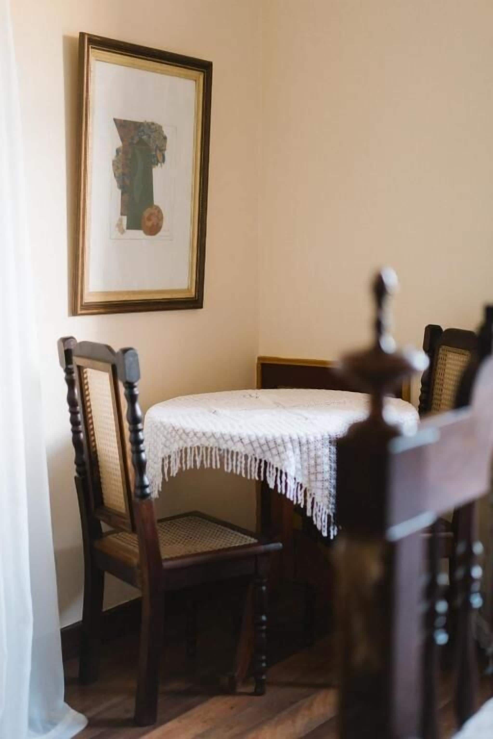 Uma sala de jantar com uma mesa redonda, duas cadeiras, um quadro na parede e piso de madeira.